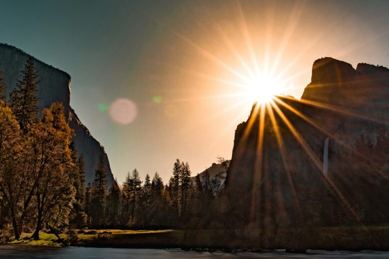 Matahari terbenam di atas pegunungan Yosemite National Park, dengan sinar matahari yang menyinari pohon-pohon dan sungai.