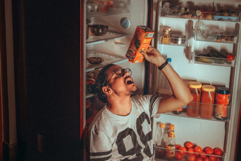 Pria mengambil minuman dari lemari es merah dalam suasana dapur yang sepi