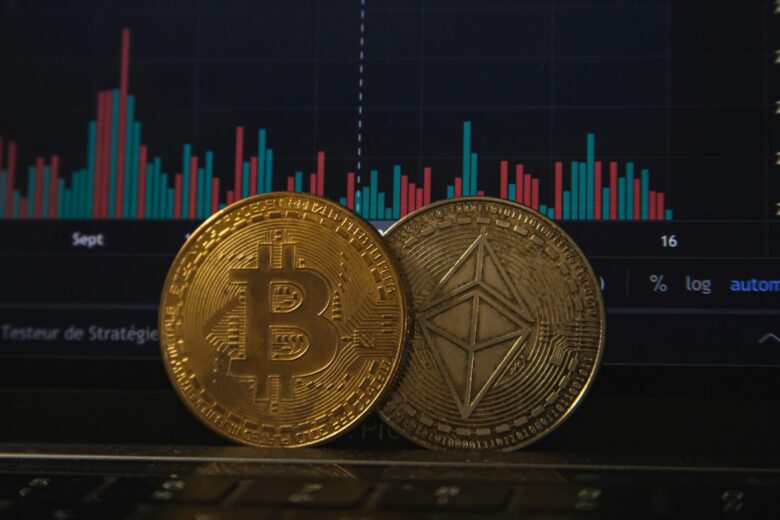 Dua koin mata uang kripto, Bitcoin dan Ethereum, diletakkan di laptop di depan grafik saham.