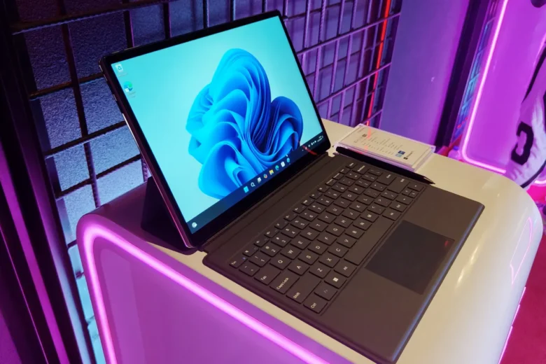 Advan Evo X 16 dengan layar Windows 11 dan keyboard terpasang di atas meja dengan pencahayaan neon.