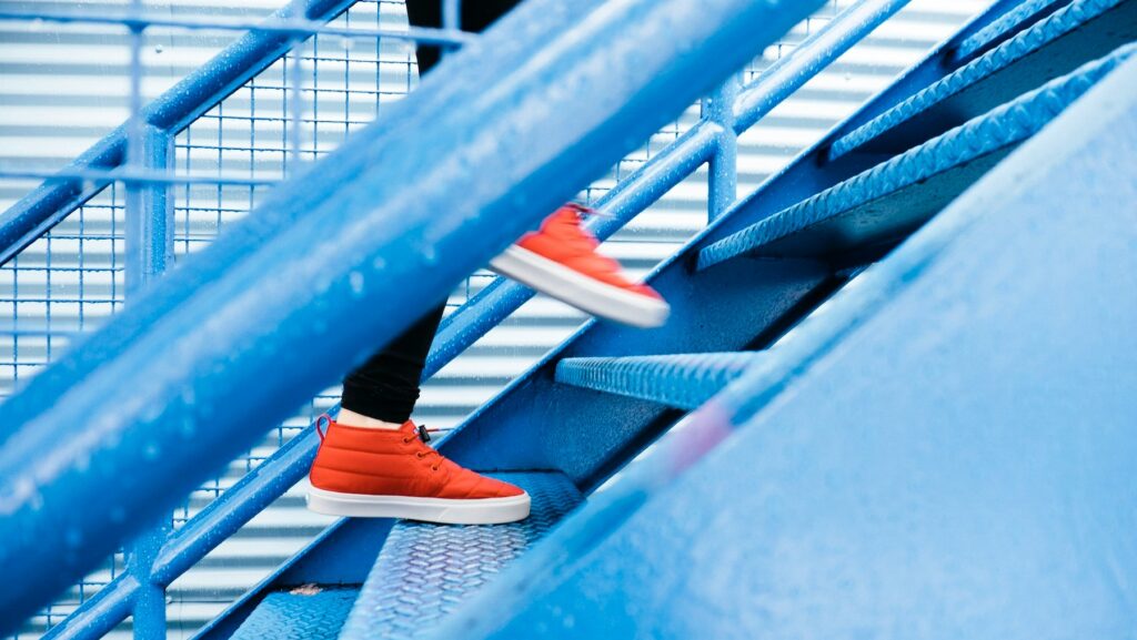 Seseorang dengan sepatu merah sedang menaiki tangga biru.