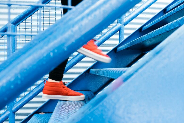 Seseorang dengan sepatu merah sedang menaiki tangga biru.