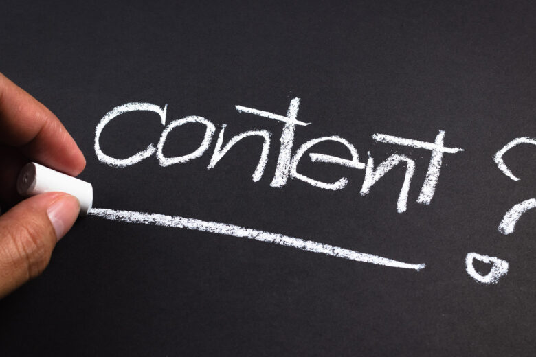 Tangan menulis kata "Content?" dengan kapur di papan tulis hitam.