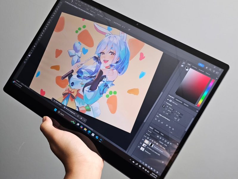 Seniman menggambar karakter anime ceria dengan Tablet Advan EVO X 16, menampilkan aplikasi desain grafis di layar.