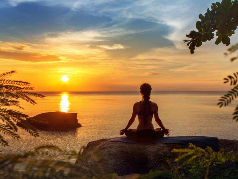 Seorang wanita meditasi di tepi pantai saat sunset yang indah