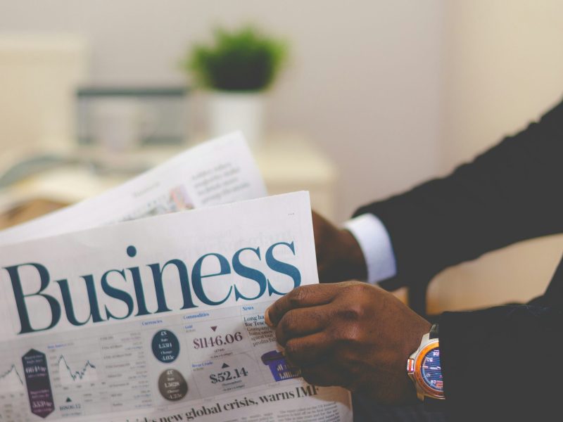 Berita Bisnis Seseorang yang mengenakan jas membaca bagian bisnis di sebuah surat kabar.