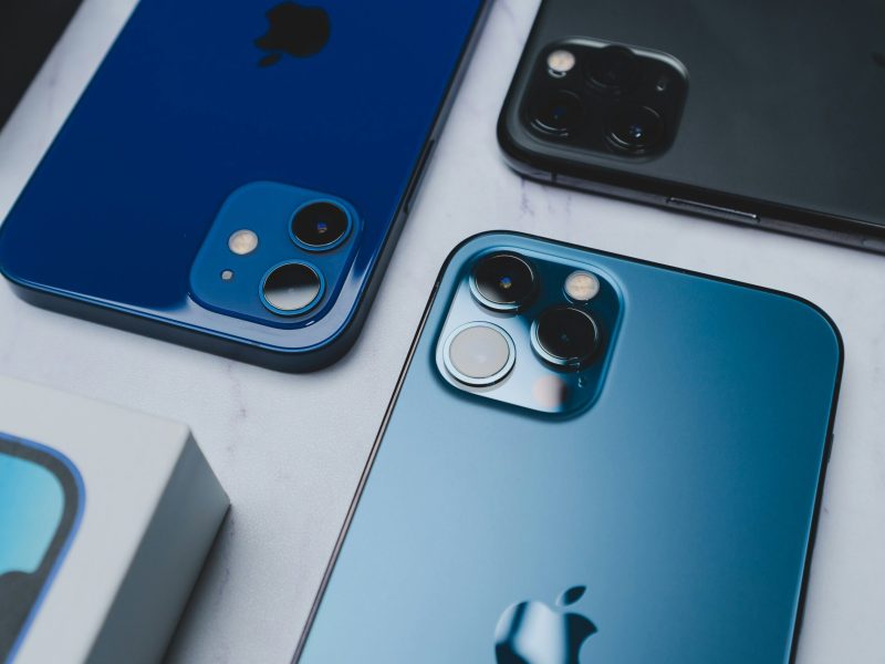 Tiga iPhone dengan warna biru berbeda dengan lensa kamera dalam fokus.