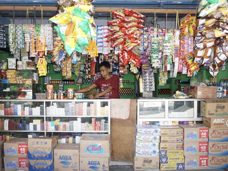 Penjual di toko kelontong dengan banyak produk yang tergantung di dinding.