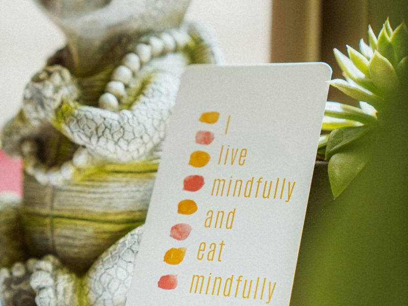 Sebuah kartu dengan tulisan "I live mindfully and eat mindfully" yang diletakkan di samping patung lucu yang mengajak untuk bersyukur.