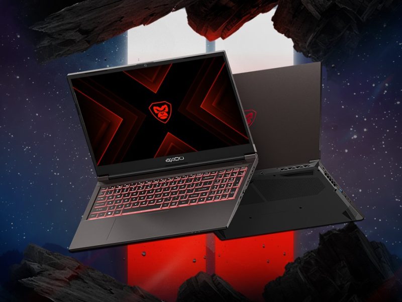 Laptop gaming hitam dengan aksen merah dan keyboard dengan lampu latar merah terletak di permukaan berbatu dengan latar belakang nebula.