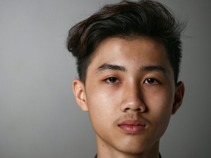 Potret Pemuda dengan Ekspresi Tenang Pemuda dengan wajah tenang dan rambut rapi di latar belakang abu-abu.