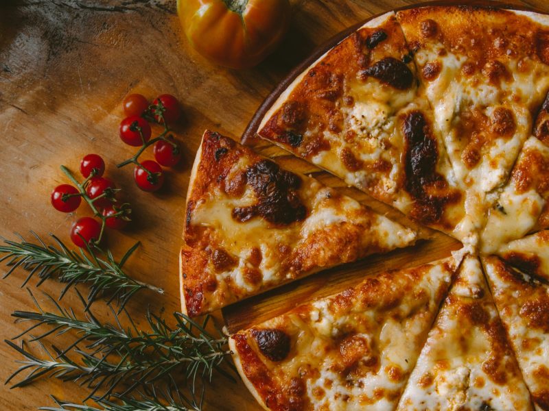 Pizza keju dengan tomat ceri dan rosemary di atas papan kayu