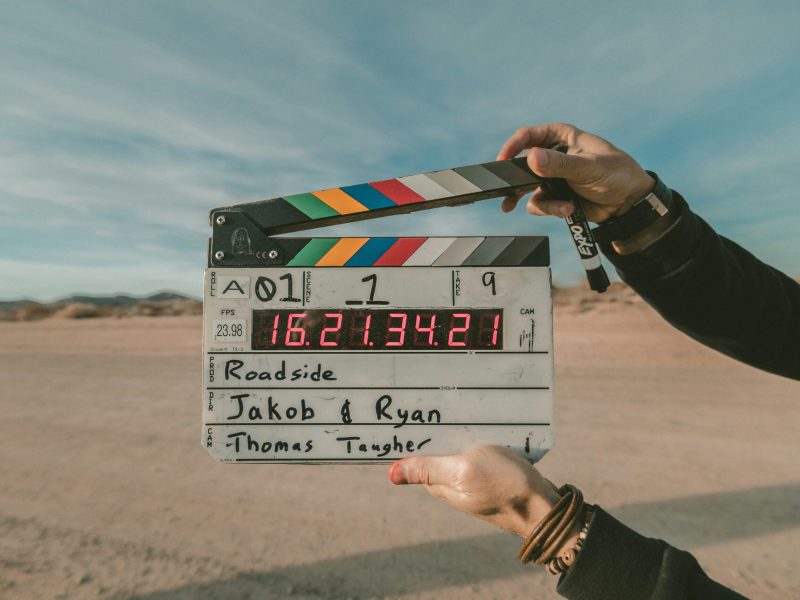 Papan clapper Papan clapper dengan informasi adegan, pengambilan gambar, dan kode waktu dipegang oleh seseorang. Teks pada papan clapper bertuliskan "A01 - 1", "Roadside", "Jakob & Ryan", dan "Thomas Taugher".
