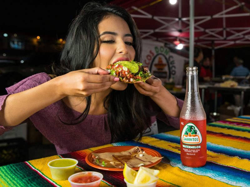 Gadis muda menikmati taco sambil memegangnya dengan tangan di sebuah restoran outdoor