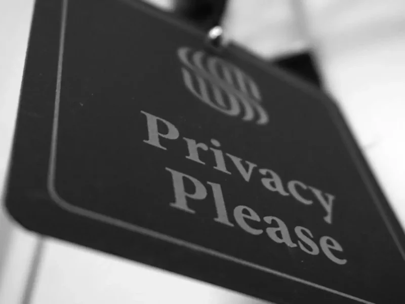 Tanda Privasi Foto hitam putih dari sebuah tanda yang bertuliskan "Privacy Please." Tanda tersebut digantung di pintu putih dan sedikit miring.