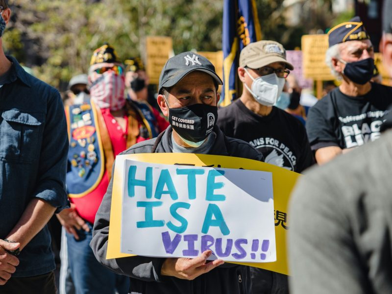 Peserta demonstrasi menahan spanduk bertuliskan 'HATE IS A VIRUS' dalam acara protes menentang diskriminasi dan kebencian.