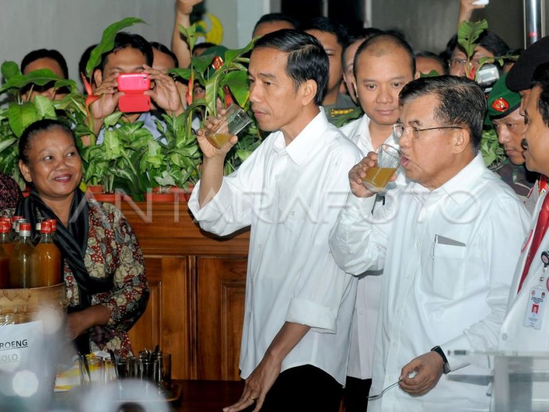 Jokowi dan Jusuf Kalla menikmati minuman di sebuah acara, dikelilingi oleh penonton.