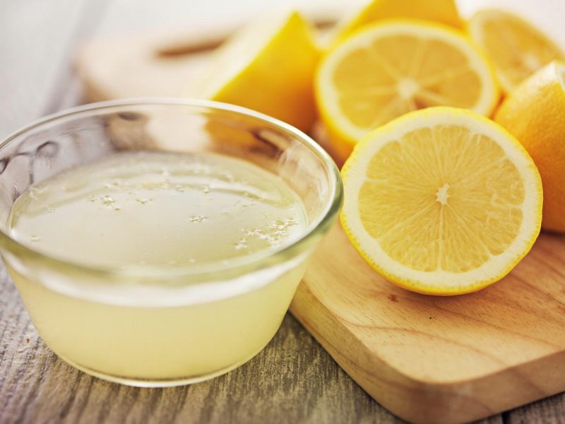 Jus lemon segar dalam mangkuk kaca Mangkuk kaca berisi jus lemon segar di sebelah beberapa irisan lemon di atas talenan kayu.