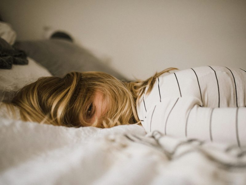 Wanita dengan rambut pirang berbaring di tempat tidur dengan selimut putih di atasnya, hanya matanya yang terlihat.