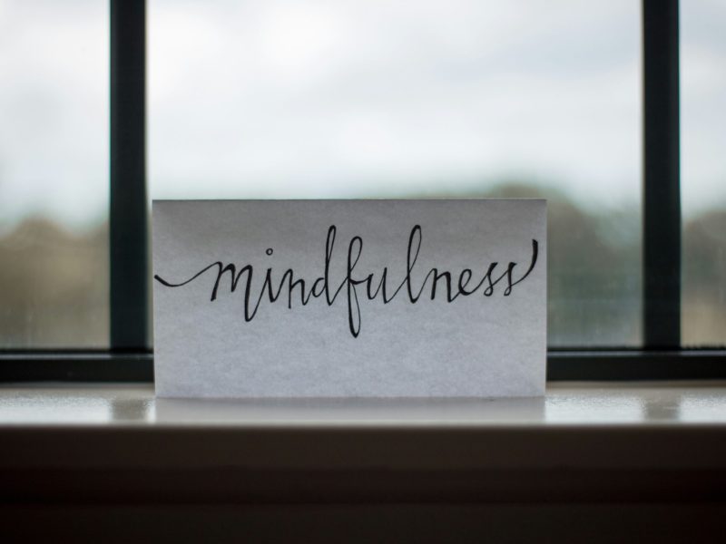 Kertas bertuliskan "mindfulness" di atas meja, dengan pemandangan di jendela.