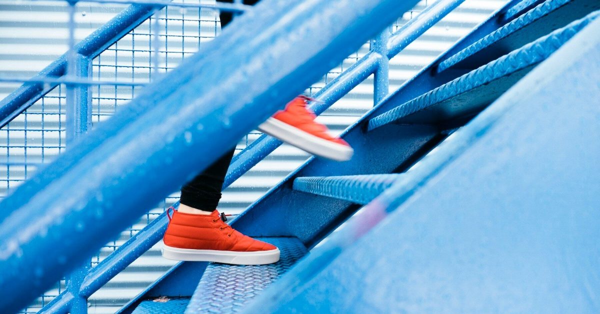 Seseorang dengan sepatu merah sedang menaiki tangga biru.