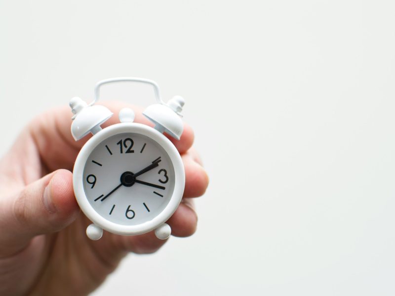 Jam Alarm Putih Jam alarm putih dengan angka hitam dipegang di tangan seseorang, waktu pada jam tersebut adalah 03:00
