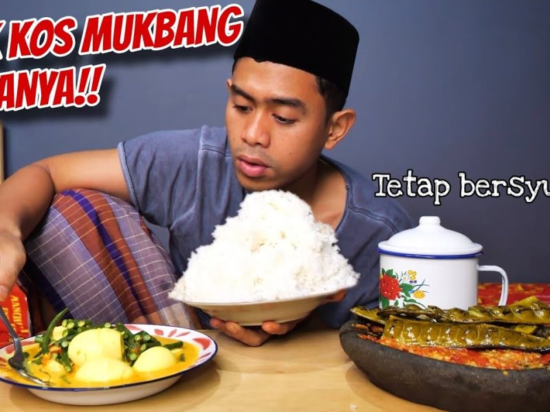 Seorang pemuda mengenakan kopiah duduk dengan piring berisi nasi besar dan makanan lainnya, menunjukkan suasana mukbang di kos.