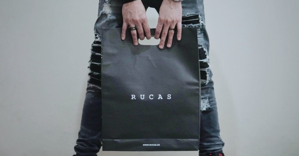 Pria memegang tas belanja berwarna hitam dengan logo RUCAS di depan