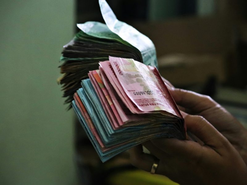 Uang Tunai Tangan seseorang memegang setumpuk uang kertas Rupiah Indonesia.