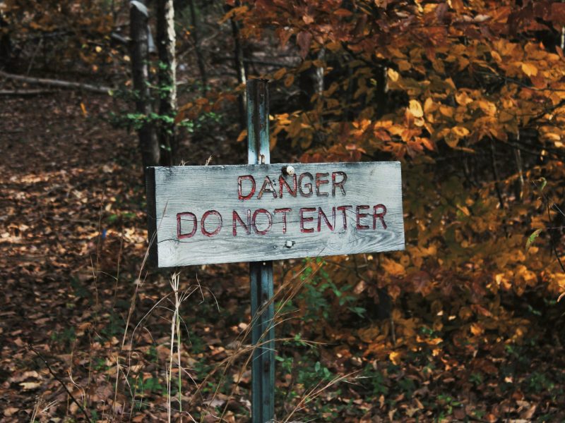 Papan Nama Bahaya di Hutan Papan nama kayu lapuk di hutan bertuliskan "BAHAYA JANGAN MASUK" dengan cat merah. Papan nama itu dipasang pada tiang logam berkarat dan dikelilingi oleh daun-daun yang berguguran.