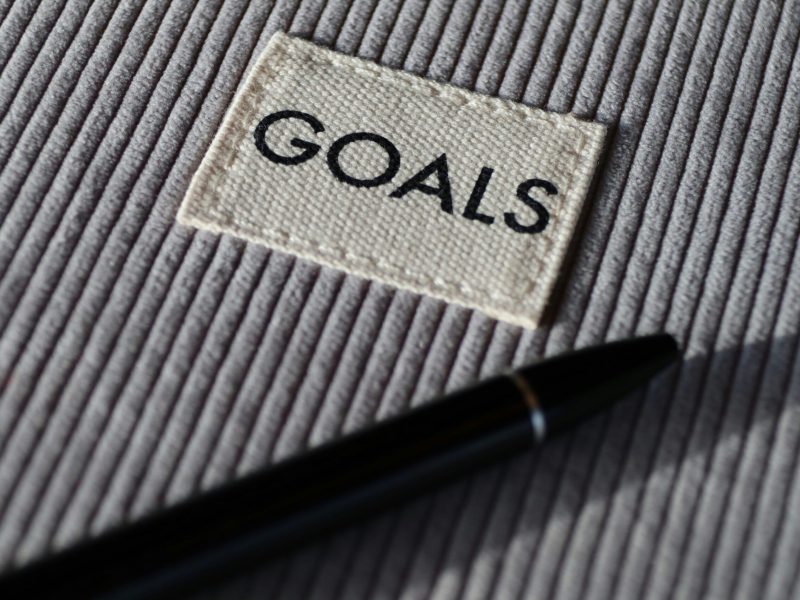 Close-up pen and tag with the word "GOALS" on a textured surface.