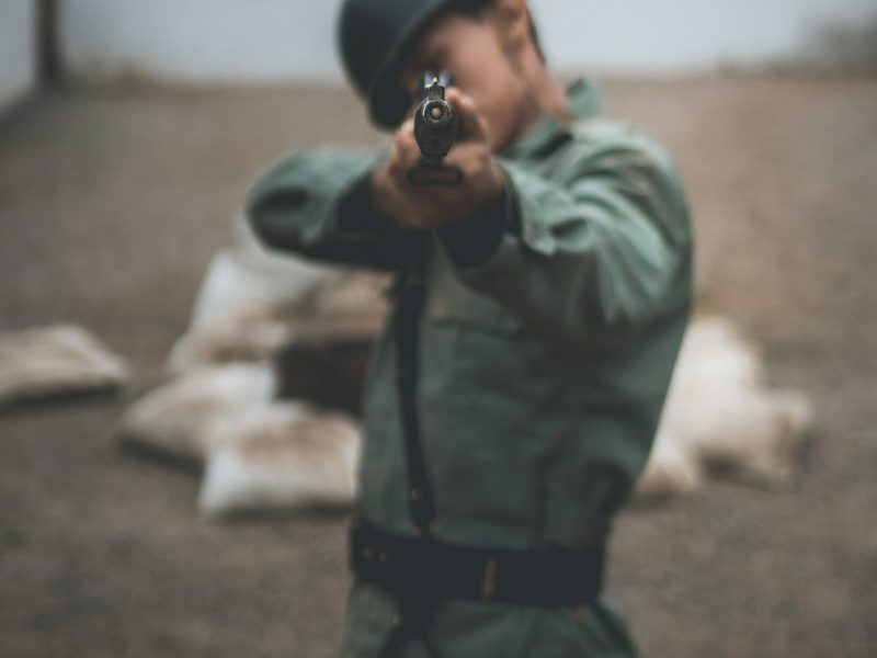 Tentara mengenakan helm dengan senjata api mengarah ke kamera dalam lingkungan latihan militer.