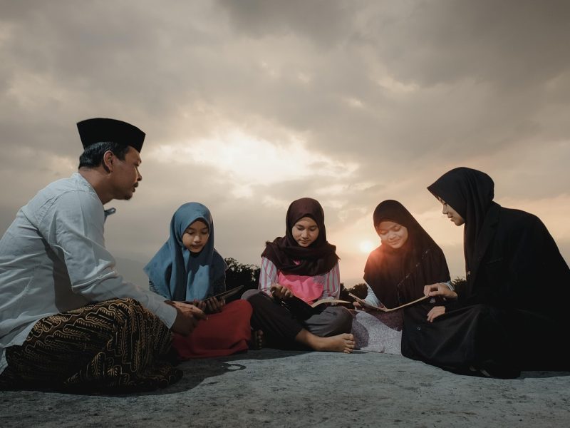 Kelompok orang sedang membaca buku di bawah langit berawan saat senja.