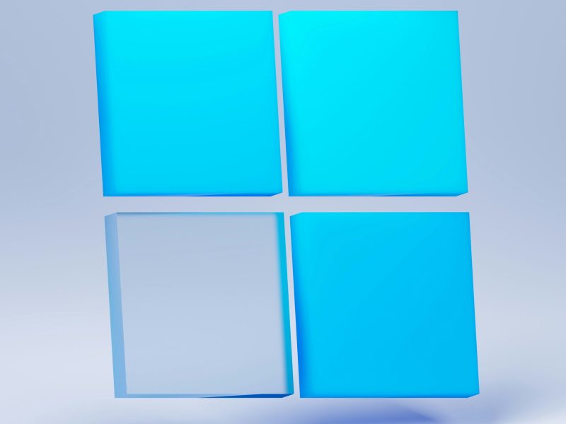 Rendering 3D logo Windows dengan warna biru muda dan latar belakang abu-abu muda.