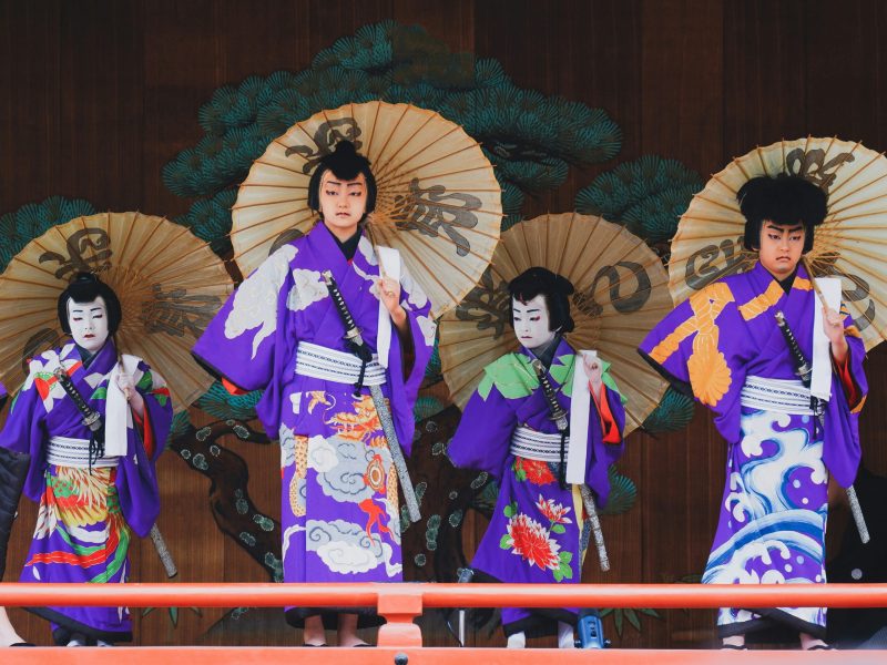 Penampil Jepang dalam Kostum Tradisional Empat orang berpakaian tradisional Jepang dengan pedang dan payung berdiri di atas panggung.