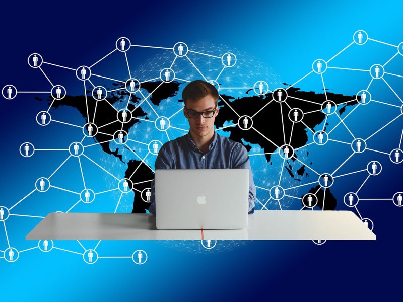 Integrasi multi-platform dalam marketing, menunjukkan berbagai saluran komunikasi yang terhubung. Seorang pria duduk di depan laptop dengan latar belakang dunia yang dihubungkan oleh jaringan.