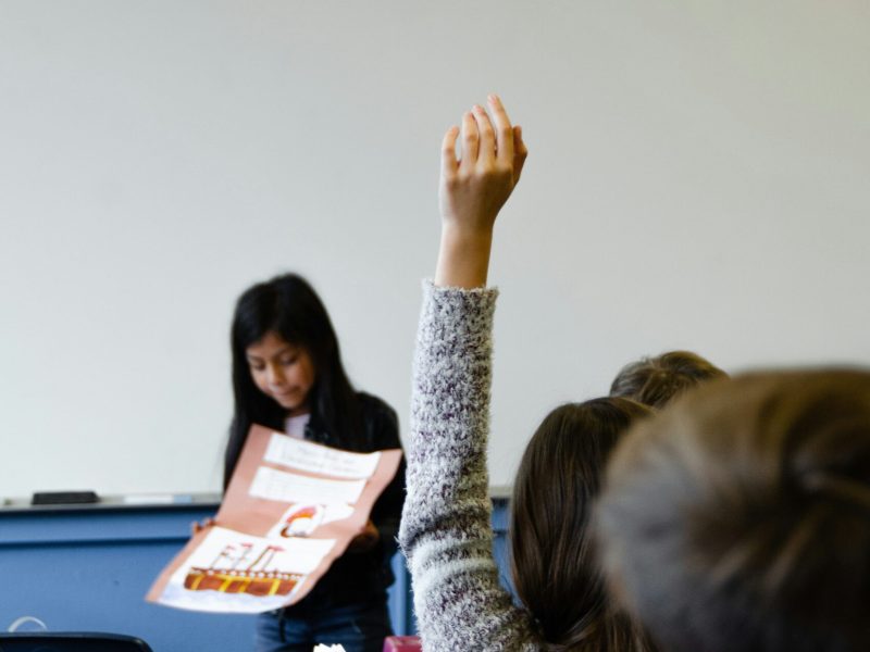 Siswa Aktif di Kelas Seorang siswa mengangkat tangan di kelas untuk berpartisipasi dalam presentasi.