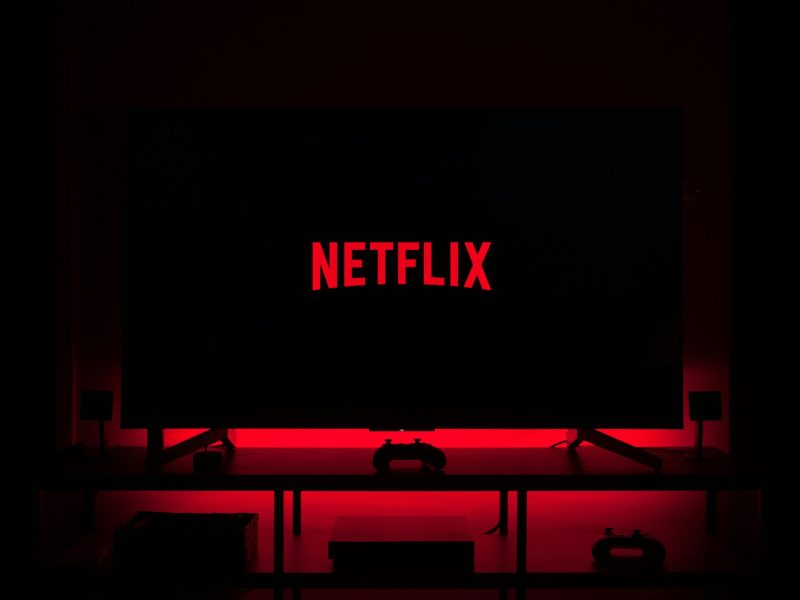 Logo Netflix yang terlihat di layar TV dengan pencahayaan merah.