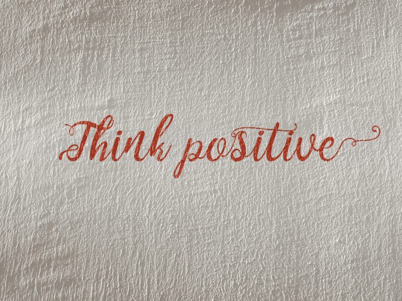 Teks "Think positive" di atas latar belakang tekstur yang berkilau.